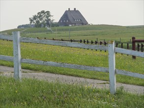 A large house stands on a hill surrounded by green fields and a white fence in the countryside,