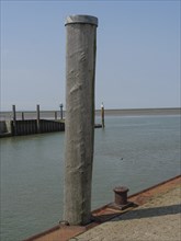 A single wooden pile at the edge of the harbour with a view of the calm sea and sky, hallig hooge,