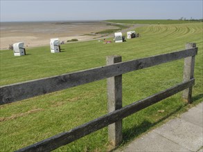 Meadow with beach chairs and a wooden fence along a path in front of a vast sandy beach and the sea