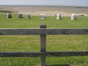 View over a green meadow with beach chairs and a wooden fence to a wide sandy beach and the sea in