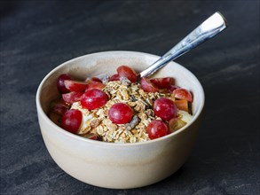 Fresh homemade muesli with organic red grapes and oat flakes in a ceramic bowl with a spoon on a