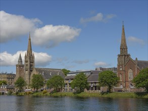 View of churches and historic buildings along a river under a clear and cloudy sky, Inverness,