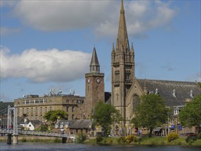 Buildings and churches with high towers on a riverside under a blue sky with some clouds,