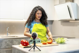 Latin young female content creator recording tutorial while cooking healthy food at home