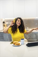 Vertical photo of a latin young woman listening to music and dancing eating breakfast at home