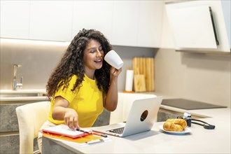 Female latin young content creator working at home while drinking coffee at morning sitting in the