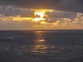 Dramatic sunset on the beach with reflections in the wet sand and cloudy sky, Juist, North Sea,