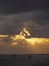 People walking on the beach during a dramatic sunset with dark clouds, Juist, North Sea, Germany,