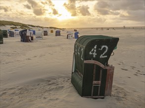 Single beach chair in the foreground on a spacious beach at sunset, Juist, North Sea, Germany,