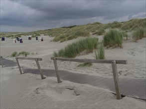 Wooden fence path through the sandy dunes with high grass under a cloudy sky, Juist, North Sea,