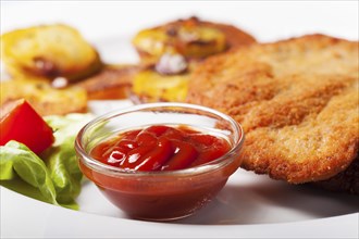 Ketchup with a Wiener schnitzel and fried potatoes