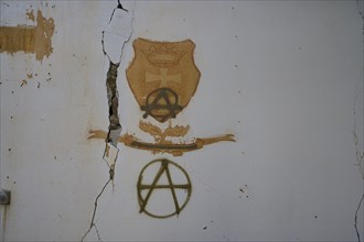 On a cracked white wall in an abandoned building, coats of arms and anarchy symbols can be seen as