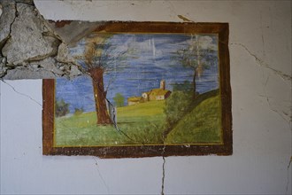 On a cracked wall of an abandoned house is a painting of a rural scene with a tree, church and