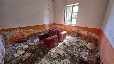 Abandoned room with worn red armchairs and orange-coloured walls. The floor is covered with dirt