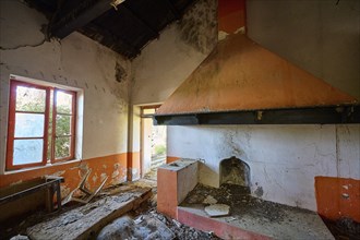 Abandoned room with a large fireplace and orange-coloured walls through which a window lets in