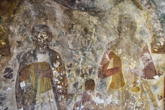 Fading frescoes on a church wall show religious figures, parents with childByzantine chapel Agios