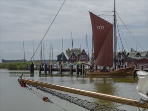 A harbour with boats and sailboat at the quay, in the background colourful houses and an overcast