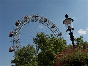 Ferris wheel and old street lamp in a park with green foliage and blue sky, Vienna, Austria, Europe