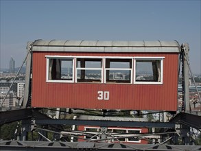 Close-up of a red cabin with the number 30 on a Ferris wheel with the city in the background,