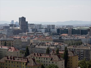 A wide city panorama with numerous buildings, rooftops and distant mountains under a slightly