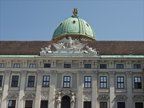 Historic baroque building with copper-green dome and roof ornaments under a clear sky, Vienna,