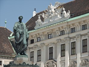 Historical statue in front of a white baroque building with reliefs and ornaments under a blue sky,