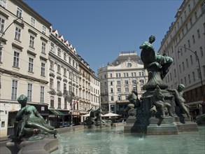 A fountain with several bronze sculptures in a square surrounded by historic buildings, Vienna,