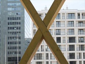 X-shaped timber constructions in front of a modern office building with large windows, Vienna,