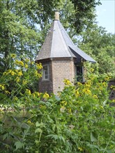 A brick tower surrounded by yellow blossoming flowers and green foliage, embedded in a summer
