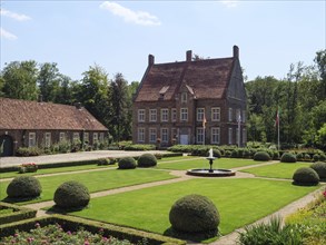 Large manor house with magnificent gardens and fountain, framed by trimmed bushes and manicured
