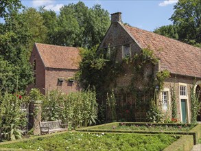 Historic property with a picturesque garden and an old brick building, overgrown with climbing