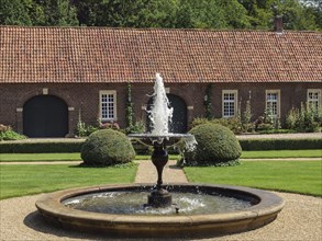 Spacious garden with central fountain, manicured lawn and an old brick building, ochtrup,