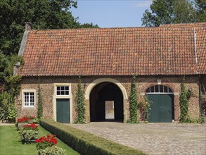 A brick barn with a red roof and courtyard gate, surrounded by a paved courtyard and garden,