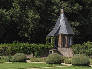 A small tower with a slate-covered roof in the middle of a well-tended garden with shrubs, green