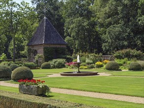 A beautiful garden with a central fountain, manicured lawn, various shrubs and flowers, surrounded