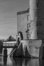 A part of a historic castle with moat, bridge and a tower, shown in black and white, gemen,