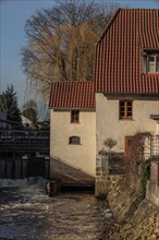 Old mill by a river with red tiled roof and bare trees in the background, gemen, münsterland,