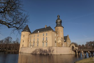 Castle with moat and striking helmet tower surrounded by winter trees on a bright day, gemen,