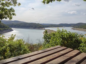 Wooden picnic bench with a view of an expansive lake and surrounding hills, surrounded by green