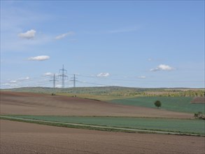 Wide fields with a few electricity pylons and a hilly forest in the background, Waldeck, Hesse,