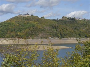 A natural lake with wooded hills stretching along the shore, under a partly cloudy sky, a peaceful