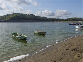 Two small boats in the water near a sandy beach, surrounded by hills under a cloudy sky, Waldeck,