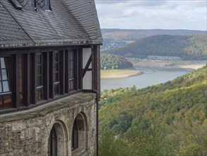 Old building with a view of a lake and surrounding hills in autumn, Waldeck, Hesse, Germany, Europe