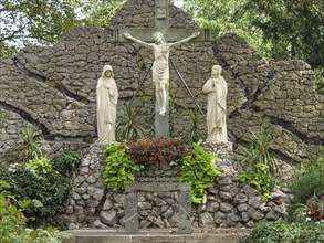 Religious site with a cross and statues of saints, surrounded by a stone wall and flowers, Werl,