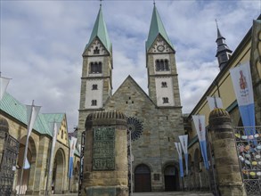 Imposing church with twin towers and main entrance, banners waving against the cloudy sky, Werl,