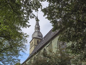 Church tower and roof section seen through trees, Gothic architecture surrounded by nature, Werl,