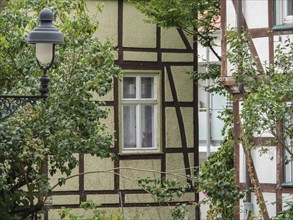 Half-timbered house with black and white façade and one window, next to a street lamp and trees,