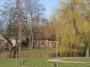 Wooden building in a rural setting with meadow and willow trees, peaceful village scene, Vreden,