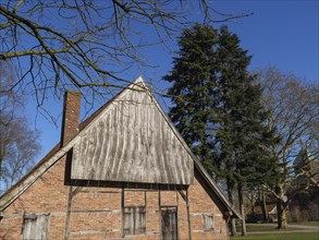 Rustic wooden hut with bare branches in the foreground, surrounded by green and bare trees under a