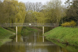 A tranquil scene of a bridge crossing a river surrounded by willows and dense green vegetation,